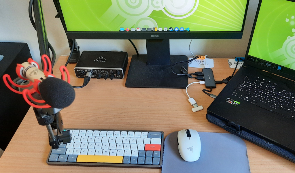 A dusty desk with a Behringer C2 microphone an UMC202HD audio interface
plugged in to a USB hub and a laptop